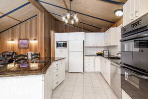 Kitchen with black appliances, vaulted ceiling, a sink, light tile patterned floors, and white cabinetry
