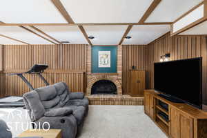 Carpeted living room featuring wooden walls, a brick fireplace, and coffered ceiling
