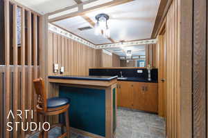 Kitchen with a sink, dark countertops, stone finish floors, brown cabinetry, and a breakfast bar