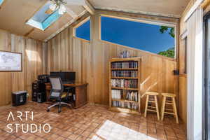 Tiled home office featuring wooden walls, a skylight, a ceiling fan, and lofted ceiling