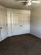 Unfurnished bedroom with dark colored carpet, a textured ceiling, a ceiling fan, a closet, and baseboards