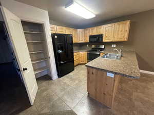 Kitchen featuring black appliances, a sink, light brown cabinetry, a peninsula, and a textured ceiling
