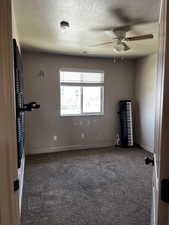 Carpeted spare room featuring a ceiling fan, a textured ceiling, a smoke detector, and baseboards