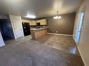 Kitchen with black appliances, a peninsula, baseboards, light brown cabinetry, and a chandelier