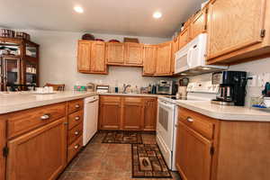 Kitchen with white appliances, a sink, light countertops, stone finish floors, and recessed lighting