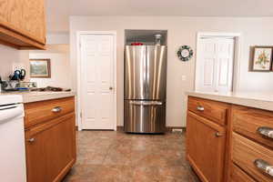 Kitchen featuring freestanding refrigerator, light countertops, brown cabinetry, and baseboards
