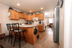 Kitchen with white microwave, freestanding refrigerator, stove, a peninsula, and light countertops
