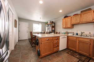 Kitchen with dishwasher, a sink, freestanding refrigerator, a peninsula, and light countertops