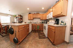 Kitchen featuring white appliances, a peninsula, light countertops, a sink, and hanging light fixtures