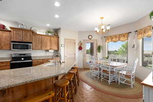 Kitchen featuring stainless steel microwave, electric range, a sink, brown cabinetry, and a kitchen bar