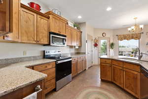 Kitchen featuring stainless steel appliances, a sink, a chandelier, brown cabinetry, and recessed lighting