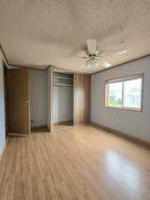 Unfurnished bedroom featuring a textured ceiling, light wood-style floors, a closet, ceiling fan, and baseboards