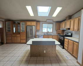 Kitchen featuring appliances with stainless steel finishes, under cabinet range hood, a textured ceiling, a sink, and a kitchen island