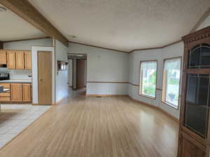 Unfurnished living room featuring light wood-type flooring, a textured ceiling, crown molding, and baseboards
