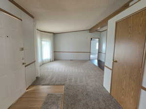 Empty room with a textured ceiling, wood finished floors, crown molding, beamed ceiling, and carpet flooring