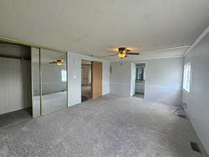 Unfurnished bedroom featuring a textured ceiling, multiple windows, carpet floors, and a ceiling fan