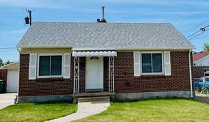 Bungalow-style house featuring brick siding, a front lawn, a shingled roof, and a detached garage