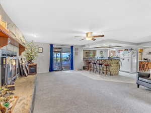 Living room with bar area, ceiling fan, light colored carpet, a textured ceiling, and light tile patterned floors