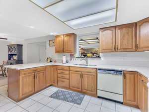 Kitchen featuring white dishwasher, a sink, a peninsula, light countertops, and light tile patterned floors