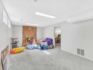 Playroom featuring carpet, a textured ceiling, a brick fireplace, an office area, and baseboards