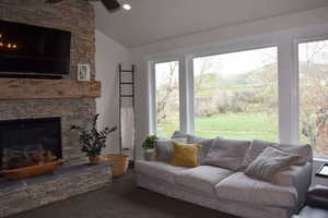 Living room with a fireplace, lofted ceiling, carpet floors, and ceiling fan