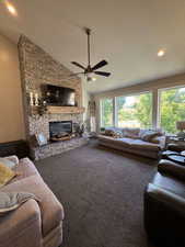 Carpeted living room with a stone fireplace, healthy amount of natural light, a ceiling fan, high vaulted ceiling, and recessed lighting