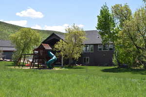 Back of house with a playground, a lawn, and a shingled roof