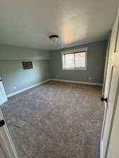 Unfurnished room featuring a textured ceiling, carpet flooring, and baseboards