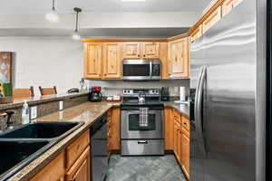 Kitchen with stainless steel appliances, a sink, a textured wall, hanging light fixtures, and dark tile patterned flooring
