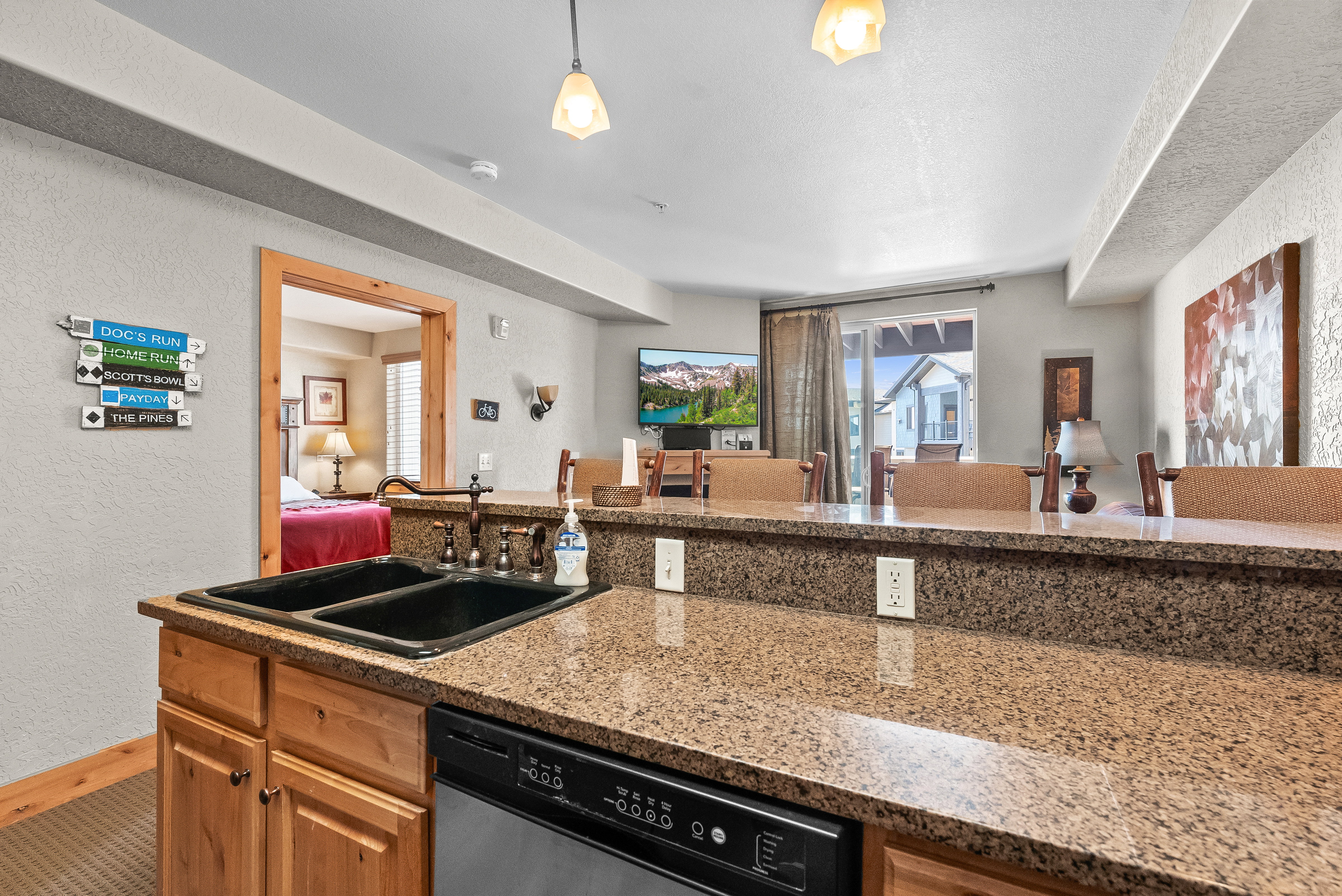 Kitchen featuring dishwashing machine, a sink, a textured wall, open floor plan, and light stone counters