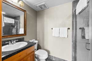 Full bathroom with vanity, a shower stall, toilet, a textured wall, and tile patterned flooring