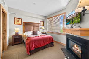 Carpeted bedroom with a glass covered fireplace, baseboards, and a textured wall