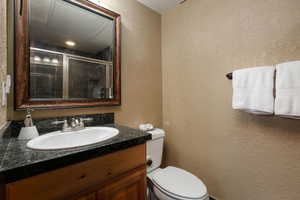Full bath with a textured wall, toilet, vanity, and tiled shower