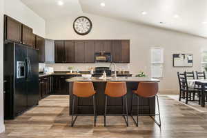 Kitchen featuring black appliances, a kitchen breakfast bar, a sink, a kitchen island with sink, and high vaulted ceiling