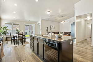Kitchen with black dishwasher, a sink, light wood-type flooring, arched walkways, and a center island with sink