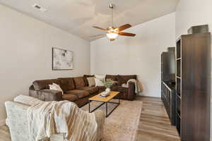 Living room with light wood-style flooring, a ceiling fan, baseboards, and lofted ceiling