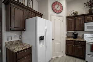 Kitchen featuring white appliances, dark brown cabinetry, and stone counters