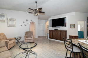 Living room featuring arched walkways, a ceiling fan, a textured ceiling, and baseboards