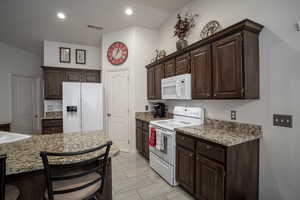 Kitchen with white appliances, dark brown cabinets, recessed lighting, and a kitchen breakfast bar
