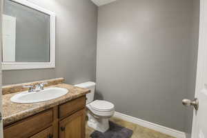 Half bath with toilet, vanity, tile patterned flooring, and baseboards