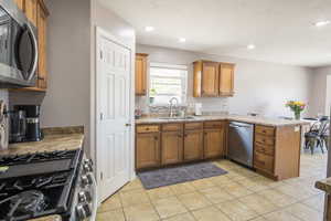 Kitchen featuring appliances with stainless steel finishes, a sink, a peninsula, brown cabinetry, and recessed lighting
