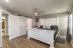 Bedroom with a barn door, light wood-style floors, baseboards, recessed lighting, and a ceiling fan