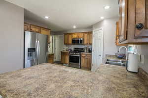 Kitchen featuring stainless steel appliances, a sink, brown cabinets, recessed lighting, and a peninsula