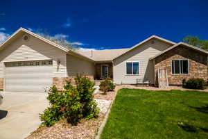 Ranch-style home featuring stone siding, an attached garage, concrete driveway, and a front lawn