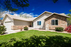 Ranch-style home featuring stone siding, an attached garage, a front lawn, and driveway