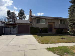 Split foyer home with a chimney, an attached garage, concrete driveway, brick siding, and stucco siding