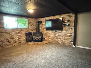 Unfurnished living room featuring a wood stove, carpet, brick wall, and baseboards