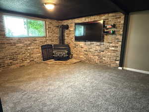 Unfurnished living room featuring a wood stove, carpet flooring, brick wall, and baseboards