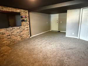 Unfurnished living room featuring carpet floors, brick wall, and baseboards