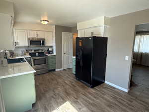 Kitchen featuring stainless steel appliances, a sink, dark wood-style floors, baseboards, and light countertops